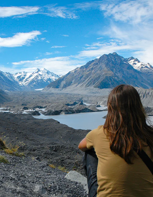 En person blickar ut över de snötäckta bergen och den vackra glaciärsjön i Aoraki/Mount Cook nationalpark, Nya Zeeland
