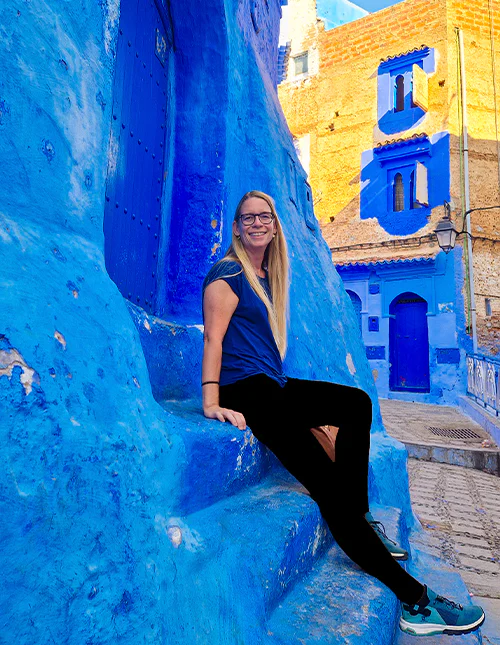 Kvinna sitter på en trappa i den blå staden Chefchaouen i Marocko