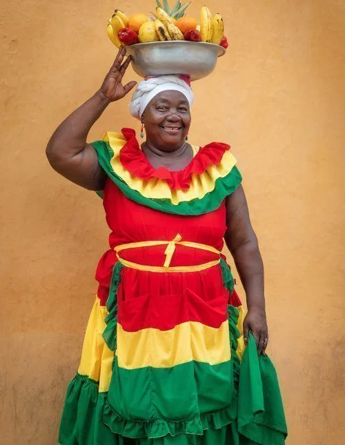 Leende colombiansk kvinna med en fruktskål på huvudet